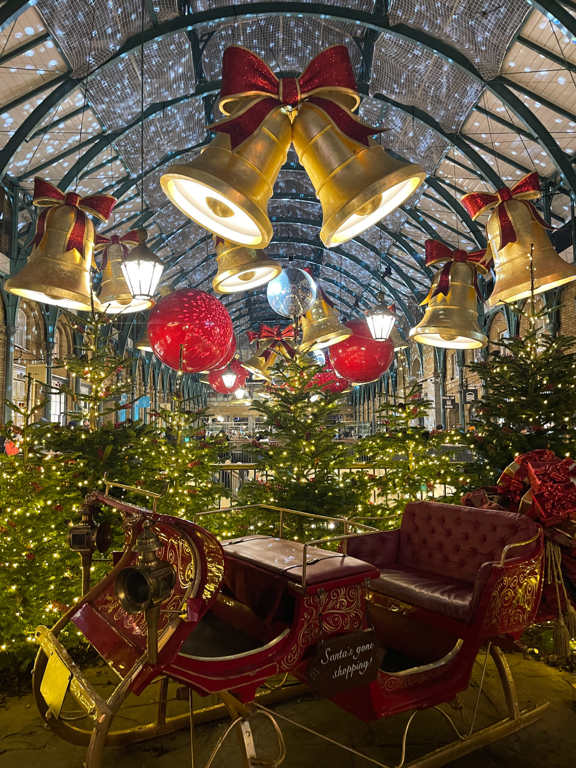 covent garden avec des cloches dorées et des rubans rouges, le traineau du père noel, des sapins lumineux et des boules rouges