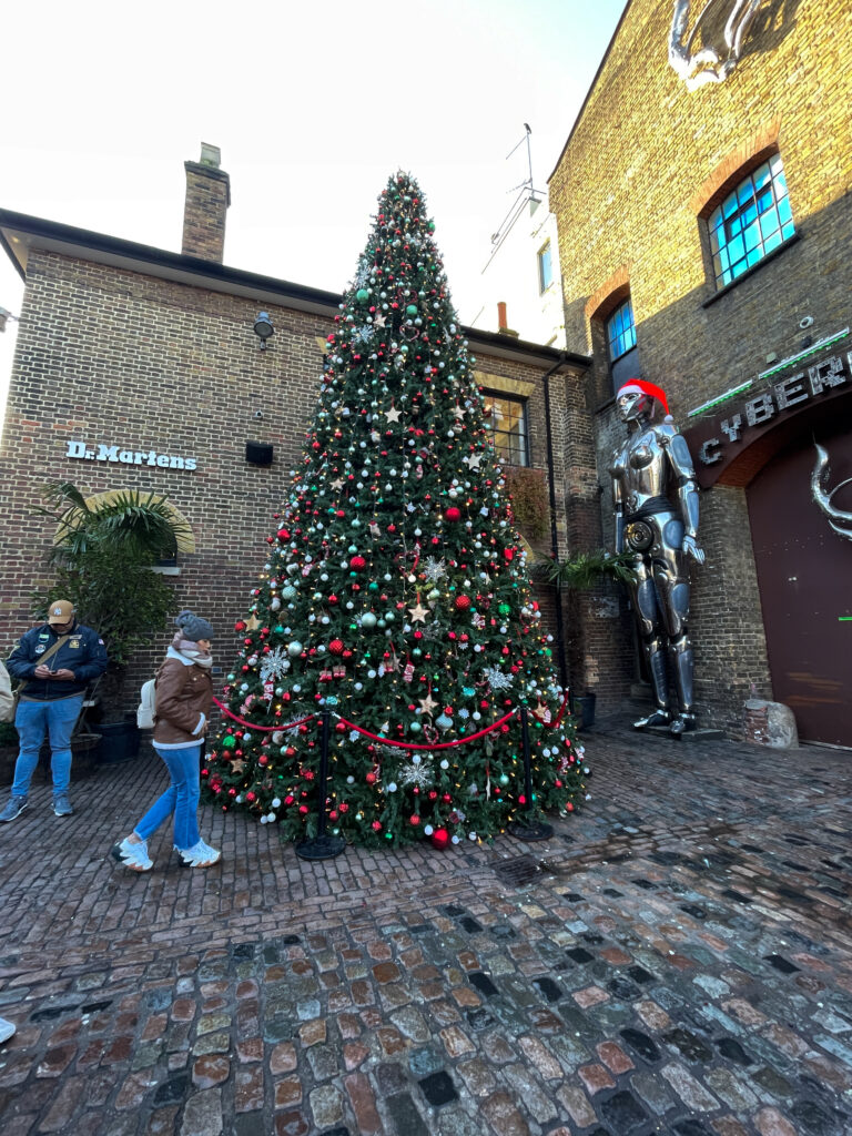 un sapin de noel décoré, avec deux personnes, deux bâtiments et une statue