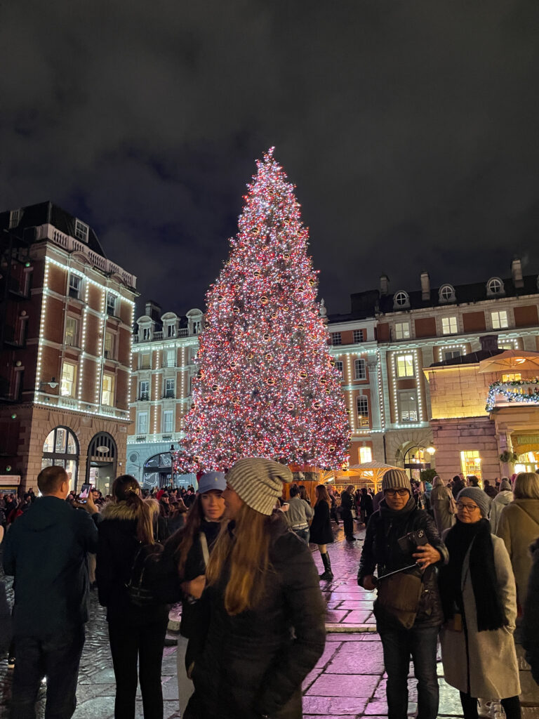 dans la rue avec une grand sapin de noel et des gens devant
