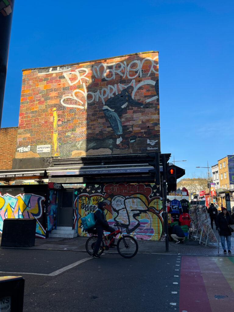 photo de rue avec une personne en vélo, un mur coloré, et des gens sur le côté