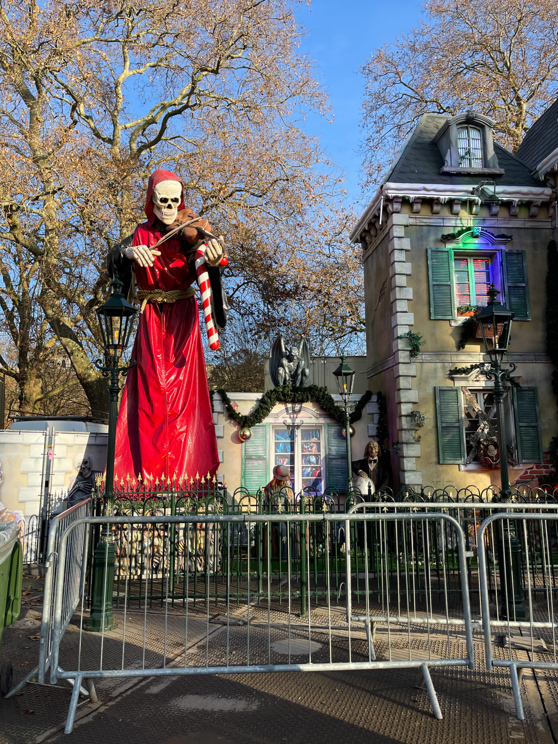 une statuette géante d'un squelette qui joue du violon, habillé en rouge avec des maisons hantées a l'arrière