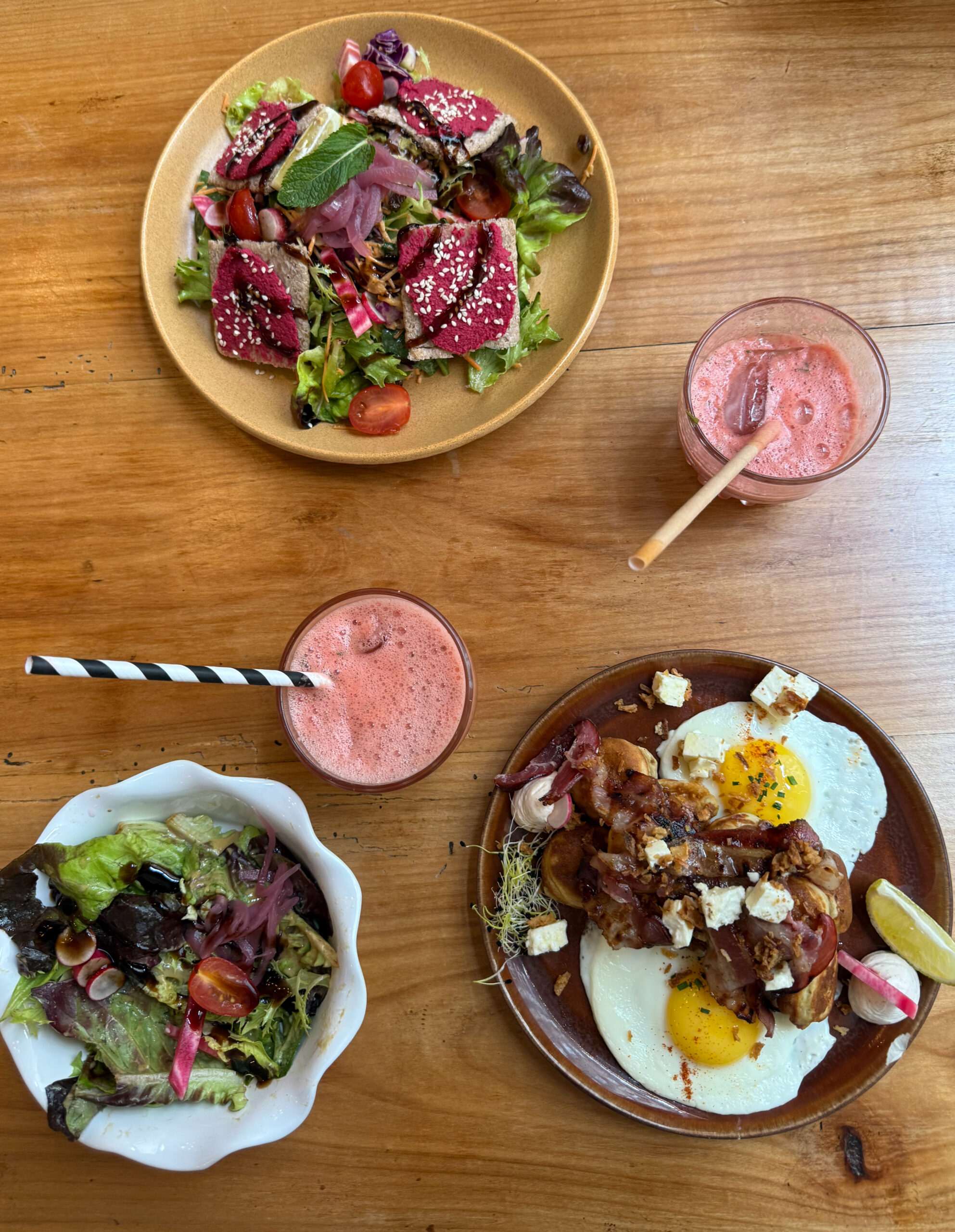 une table avec deux boissons, et trois assiettes composées d'oeufs, bacon, salade, betterave