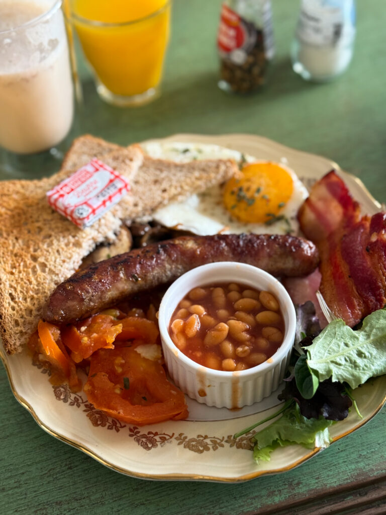 une assiette avec saucisses, haricots, tomates, oeuf sur le plat, pain et beurre.